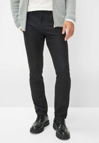 Pantalons slim-fit noirs en tissu extensible, avec un design classique à cinq poches et une texture lisse. Associés à des chaussures noires.