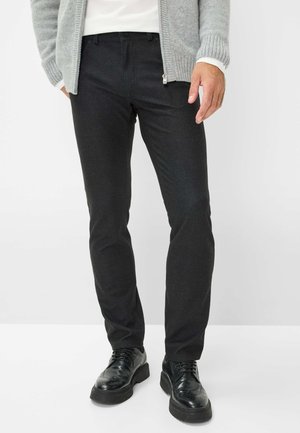 Schwarze Slim-Fit-Hosen aus dehnbarem Stoff, mit einem klassischen Fünf-Taschen-Design und einer glatten Textur. Kombiniert mit schwarzen Schuhen.