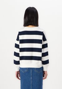 Randig tröja med marinblå och vita horisontella ränder, mjukt bomullsmaterial, rund halsringning och uppvikta långa ärmar, bärs med en denimkjol.