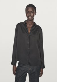 Czarna satynowa koszula zapinana na guziki z długimi rękawami, kołnierzykiem i luźnym krojem. Posiada błyszczące guziki oraz gładką, połyskującą teksturę.