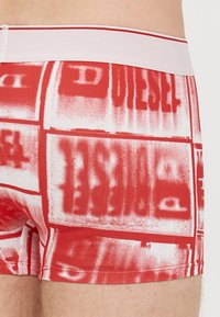 Boxer rossi con fascia elastica bianca in vita, caratterizzati da motivi testuali ripetuti. Il tessuto ha una texture liscia e un design aderente.