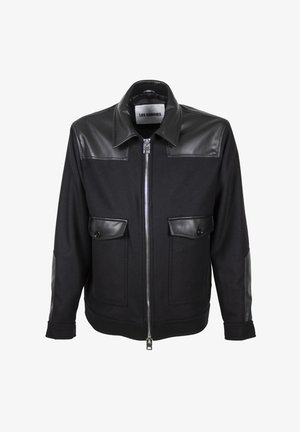 Giacca nera con cerniera, colletto in pelle, pannelli sulle spalle, patte delle tasche e toppe sui gomiti, con etichetta "Les Hommes" all'interno del colletto.