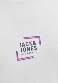 Tissu blanc avec texte noir "JACK & JONES" et "ESTABLISHED IN 1990" encadré par des lignes d'angle rouges et bleues.