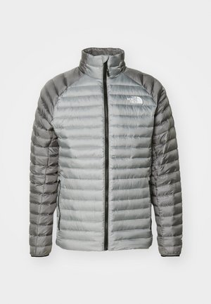 Veste rembourrée grise, avec un col montant, une fermeture éclair intégrale et un mélange de textures lisses et matelassées. Logo sur la partie supérieure gauche de la poitrine.