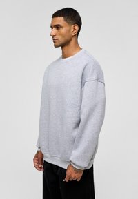 Grijze sweatshirt met een ronde hals, verlaagde schouders en geribde mouwen. Gemaakt van zachte stof, heeft een losse pasvorm en een effen textuur.