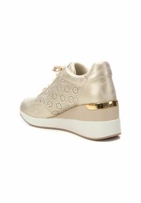Sneaker beige con design floreale perforato, texture liscia, chiusura con lacci e tacco a zeppa accentuato da una banda dorata. Suola in gomma bianca.