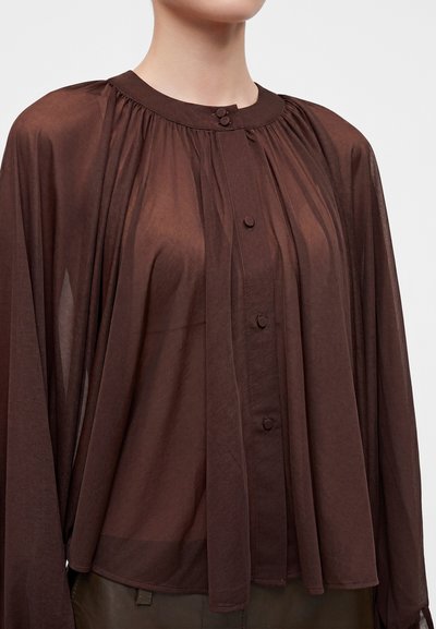 Blouse marron transparente à manches longues avec boutons recouverts de tissu et col froncé, portée par une personne des épaules à la taille.