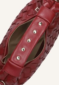Rode geweven leren handtas met een ritsluiting. Beschikt over een brede schouderband met drukknoopjes en een gladde voering aan de binnenkant. Gecombineerde textuurdetails.