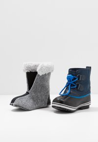 Stivale grigio in feltro con bordo in pelliccia sintetica a sinistra, e stivale impermeabile blu navy con dettagli blu e suola in gomma a destra.