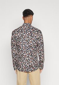 Chemise à manches longues à motif floral sur fond noir, ornée de fleurs multicolores. En coton, légèrement cintrée, avec des manches à poignet.