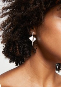 Boucles d'oreilles en argent avec une forme unique de losange allongé et des accents courbes. Le design comprend une attache à puce et une finition élégante.