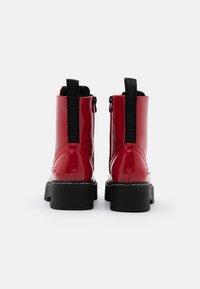Stivaletti alla caviglia in pelle verniciata rossa con suola nera spessa e robusta, dotati di cerniera laterale e tirante con marchio in rilievo sul retro.
