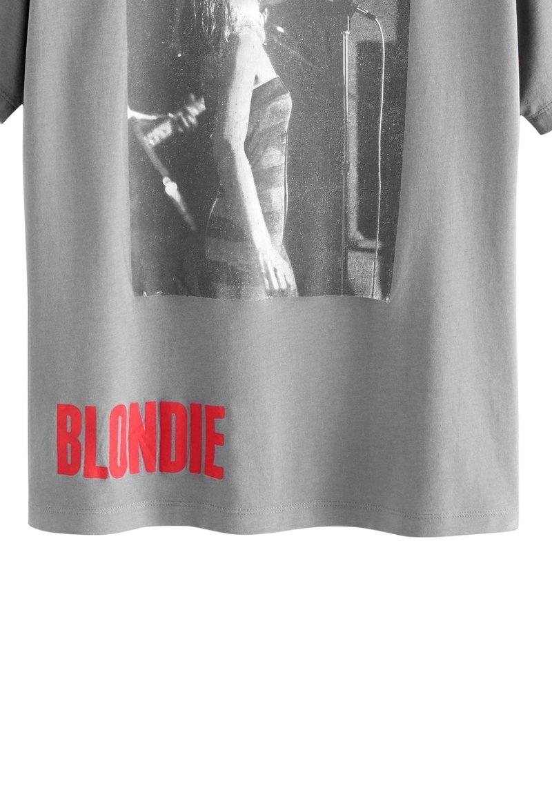 Photo en noir et blanc d'une femme chantant au micro avec un texte rouge "BLONDIE" en dessous sur un t-shirt gris.