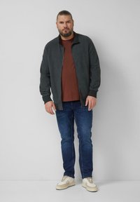 Gray zip-up jacket with textured pattern, worn over a brown t-shirt, paired with blue jeans and white sneakers. Simple, relaxed fit.