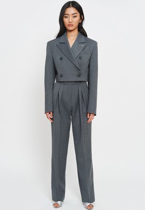 Szary dwurzędowy garnitur z teksturowanej tkaniny, z kurtką o skróconym kroju, spodniami z szerokimi nogawkami i plisami oraz czarnymi guzikami. Srebrne sandały.