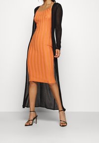 En orange randig midi-klänning gjord av ett stretchigt material, lager-på-lager med en genomskinlig svart lång cardigan. Har tunna axelband och öppen front.