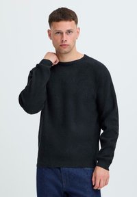 Zwarte lange mouwen trui in een gebreide textuur, voorzien van een ronde halslijn en geribde manchetten, gecombineerd met blauwe denim jeans.