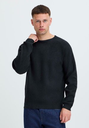 Zwarte lange mouwen trui in een gebreide textuur, voorzien van een ronde halslijn en geribde manchetten, gecombineerd met blauwe denim jeans.
