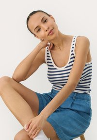 Striped tank top in navy and white, paired with a denim skirt. The fabric appears stretchy and soft, with a smooth texture and scoop neckline.