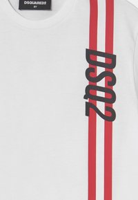Witte shirt met twee verticale rode strepen en zwarte "DSQUARED2" tekst langs de rechterkant, maat 8Y label bij de kraag.