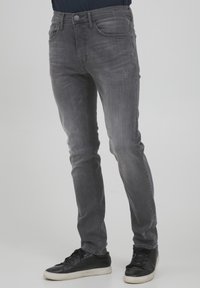 Jeans de denim gris con un corte ajustado, ligero desgaste en la parte frontal y diseño de cinco bolsillos. Combinados con zapatillas negras.