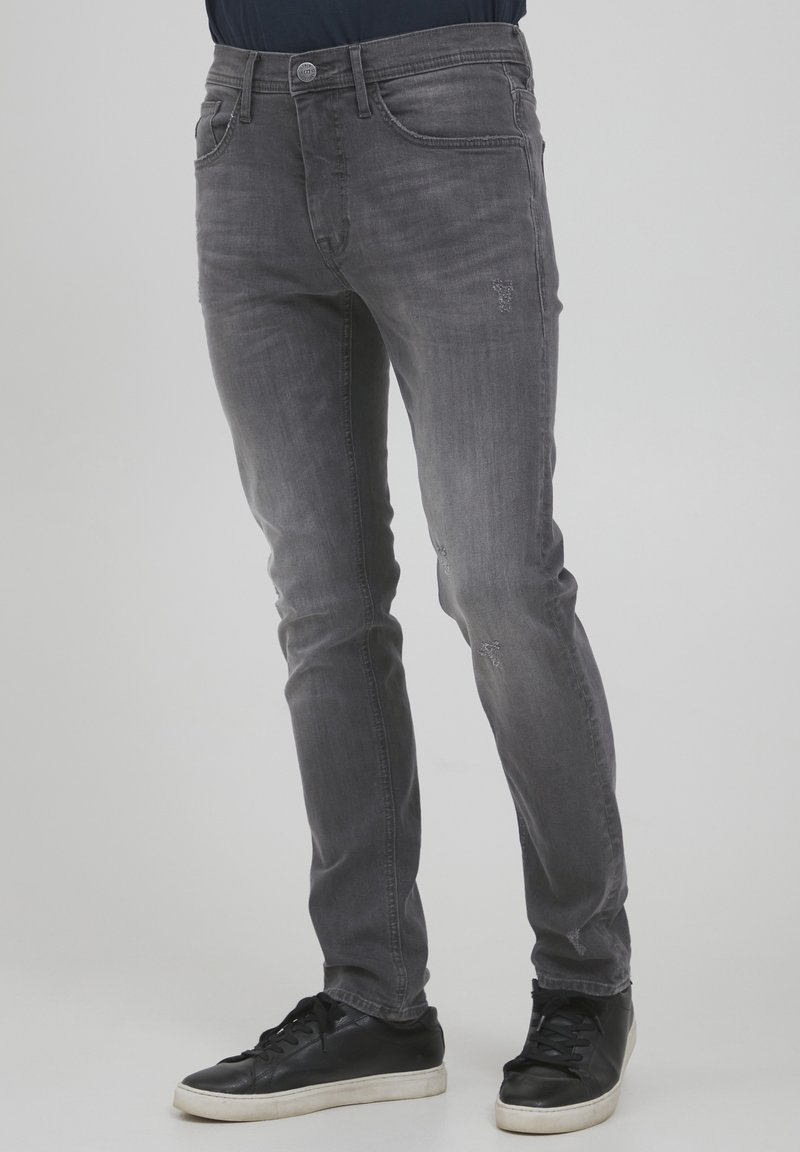 Jeans de denim gris con un corte ajustado, ligero desgaste en la parte frontal y diseño de cinco bolsillos. Combinados con zapatillas negras.