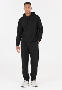 Zwarte hoodie met een voorzak en koordje, gecombineerd met bijpassende joggingsbroek. Soepele stoftextuur, ontspannen pasvorm, met lichte accenten.