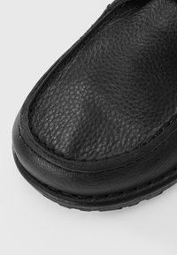 Black leather shoe showing a textured surface, rounded toe, and visible stitching along the edges. Smooth finish with durable sole construction.