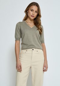 Maglia a V verde oliva in maglia con maniche corte, abbinate a jeans beige chiaro a vita alta. Design semplice, texture morbida, dettagli minimi.
