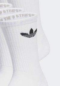 Baltie kokvilnas zeķes ar ribota tekstūra, ar melnu Adidas logotipu augšpusē un ruļļa augšdaļu.