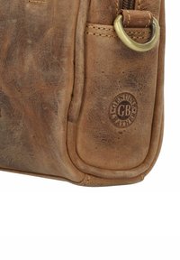 Sac à main en cuir marron avec une texture lisse, forme arrondie, coutures visibles et une boucle en laiton. Estampillé "Cuir véritable" sur le côté.