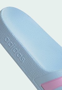 Light blue slide sandal made of textured material; features a pink accent stripe and embossed "adidas" logo on the side.
