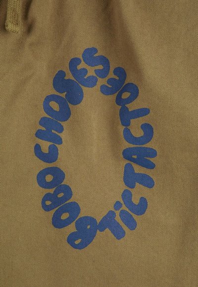 Il tessuto beige presenta un audace testo blu disposto in un motivo circolare, con lettere arrotondate e giocose, su uno sfondo di cotone texturizzato.