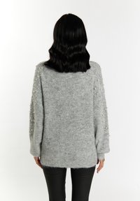 Maglione grigio lavorato a maglia con una vestibilità rilassata, caratterizzato da dettagli in perle sulle spalle e polsini a coste. Texture morbida e orlo posteriore più lungo.