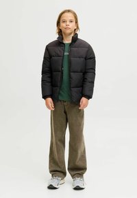 Sort quiltet pufferjakke med høj krave, båret over en grøn skjorte. Parret med brede brune corduroy-bukser og grå sneakers.