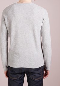 Hellgrauer Pullover aus weichem Material, mit langen Ärmeln und rundem Halsausschnitt, getragen mit dunklen Jeans.