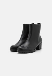Botines de cuero negro con un acabado suave, punta redondeada y un tacón grueso. Cuentan con una suela texturizada para mayor tracción.
