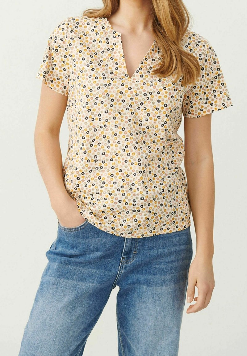 Lys gul bluse med v-hals, korte ærmer og et blomster mønster i sort, orange og hvidt. Blødt stof, lidt løs pasform.