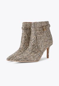 Stivaletti beige e dorati con punta affusolata, ricoperti di brillanti decorazioni, con colletto curvo e tacco sottile.