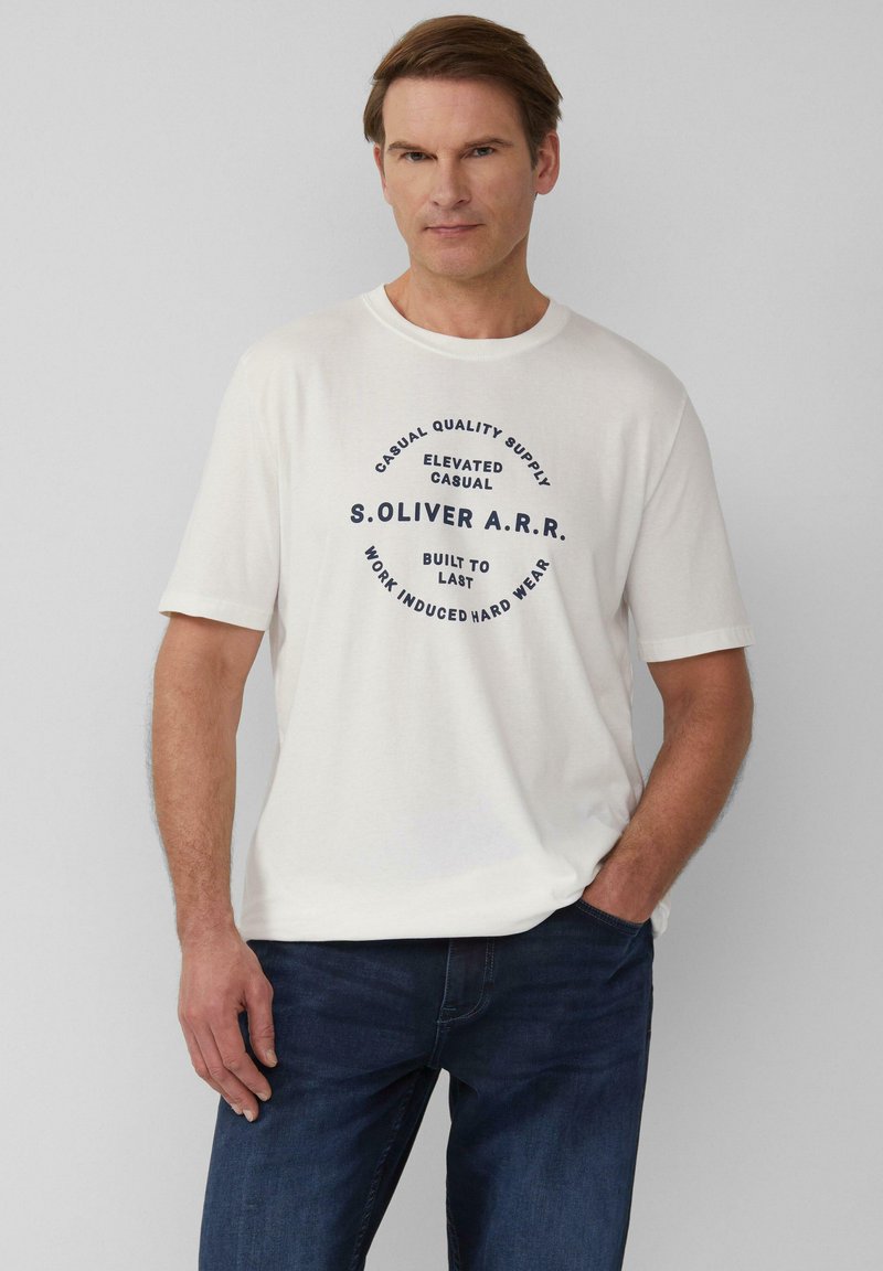Witte katoenen T-shirt met korte mouwen, voorzien van een cirkelvormig marineblauw grafisch tekstontwerp in het midden. Gedragen met marineblauwe spijkerbroek.
