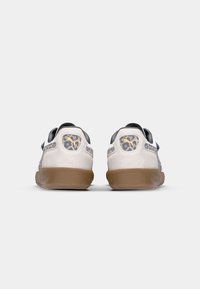 Zapatillas con parte superior blanca, acentos en negro y suela de goma. La parte trasera presenta paneles de estampado de leopardo y un detalle de logo distintivo.