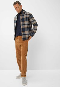 Geruite flanellen overhemd in marineblauw, grijs en amber, gecombineerd met roestkleurige corduroy broek, afgewerkt met lichtgrijze sneakers.