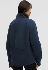 Navy blue sweatshirt with a high collar, curved seams, and ribbed cuffs. Features a logo on the back and a loose fit design. Soft texture.