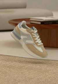 Αθλητικό παπούτσι σε μπεζ και ανοιχτό μπλε χρώμα με υλικά από δίχτυ και σουέτ, στρογγυλεμένη μύτη, κλείσιμο με κορδόνια και λογότυπο στο πλάι.