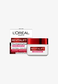 L'Oréal Revitalift fuktighetskräm i en genomskinlig burk med ett rött lock. Förpackningen har svart och röd text som beskriver anti-åldrande och parfymfria egenskaper.