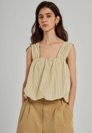 Geel gestreepte mouwloze top met brede banden, gathered lijfje en een losse pasvorm. Gecombineerd met hoog getailleerde beige broek.