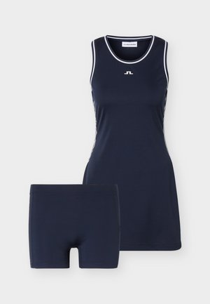 Robe de sport sans manches bleu marine avec bordure blanche et short ajusté bleu marine assorti sur fond uni.