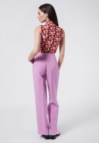 Top floral en tela roja y rosa, combinado con pantalones de tiro alto y pierna recta en rosa claro. Los zapatos son negros con un tacón grueso.