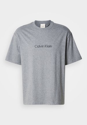 T-shirt grigia in cotone con maniche corte, scollo rotondo e logo stampato "Calvin Klein" in una tonalità più scura sul petto.
