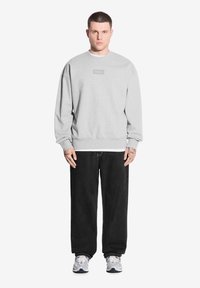 Szara bluza z okrągłym dekoltem i ściągaczami na rękawach, w połączeniu z luźnymi czarnymi dżinsami oraz sportowymi butami w wielokolorowym wzorze.